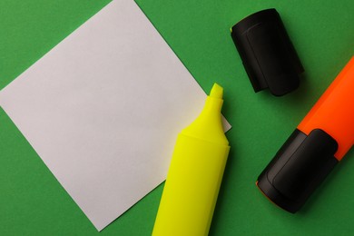 Photo of Bright color markers and sticky note with drawn arrow on green background, flat lay