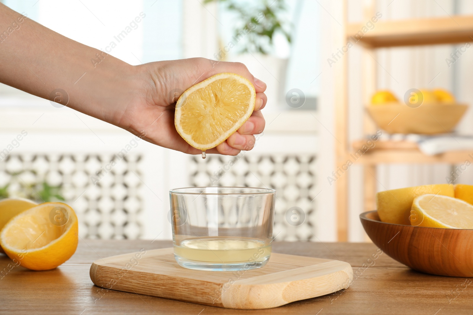 Photo of Woman squeezing lemon juice into glass bowl at table