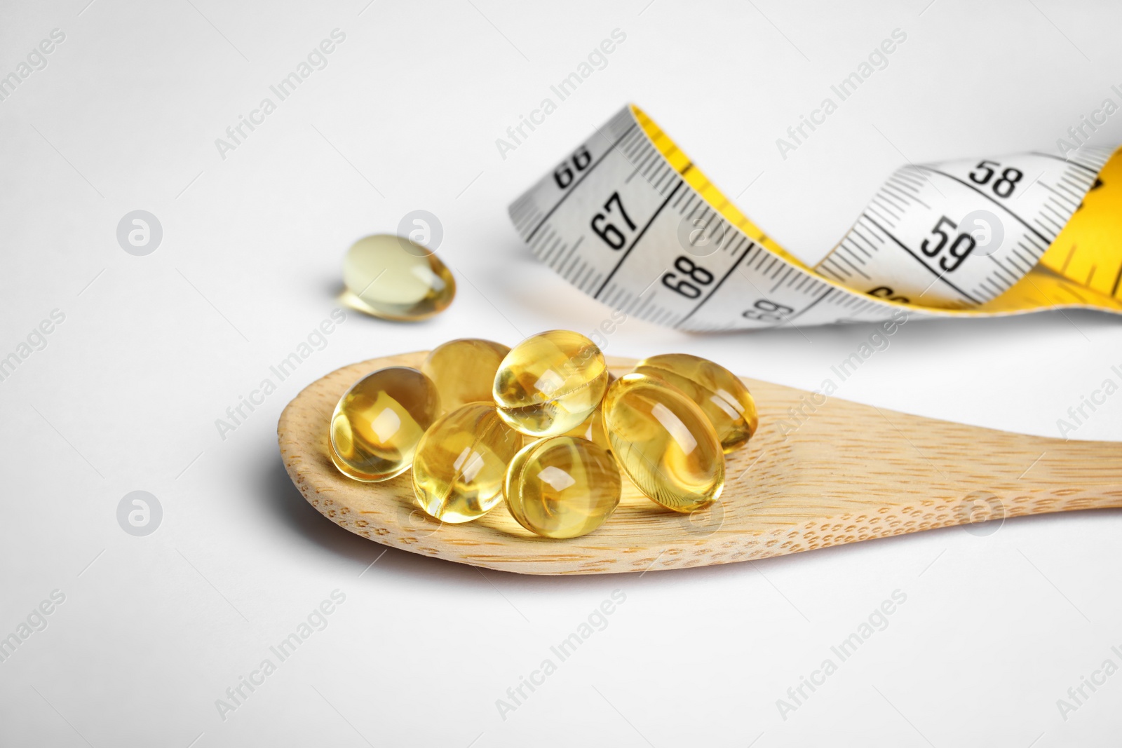 Photo of Spoon with cod liver oil pills and measuring tape on white background