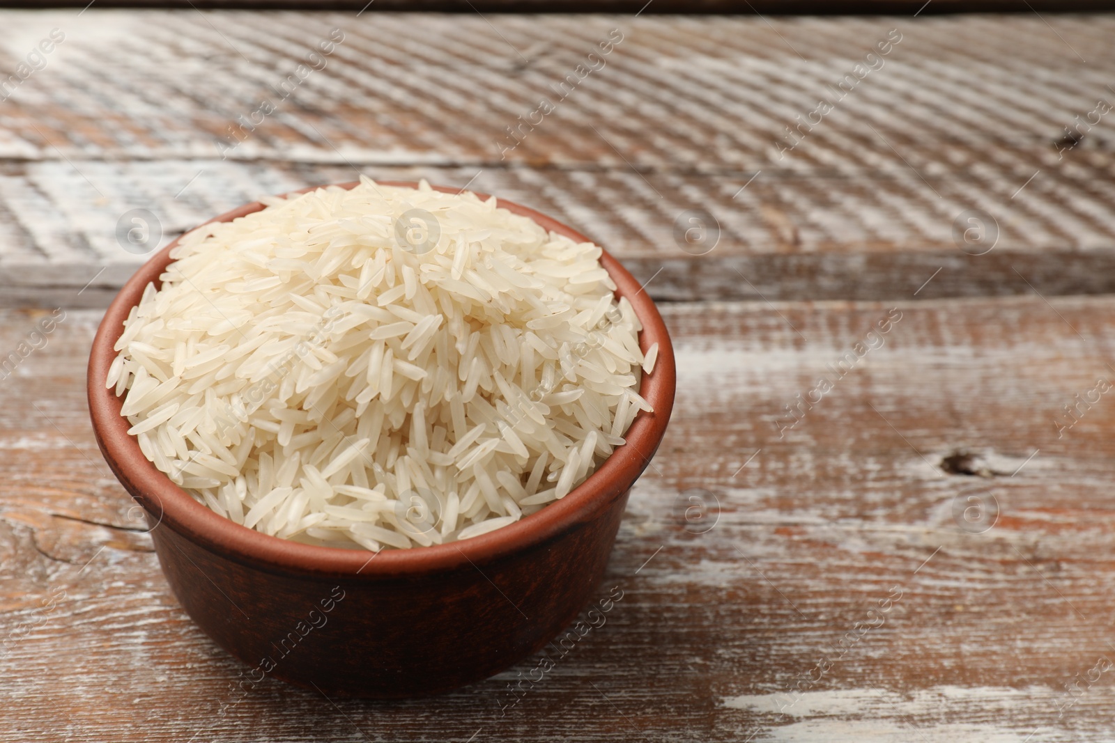 Photo of Raw basmati rice in bowl on wooden table, space for text