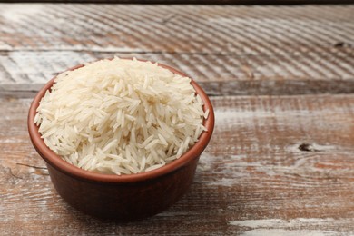 Photo of Raw basmati rice in bowl on wooden table, space for text