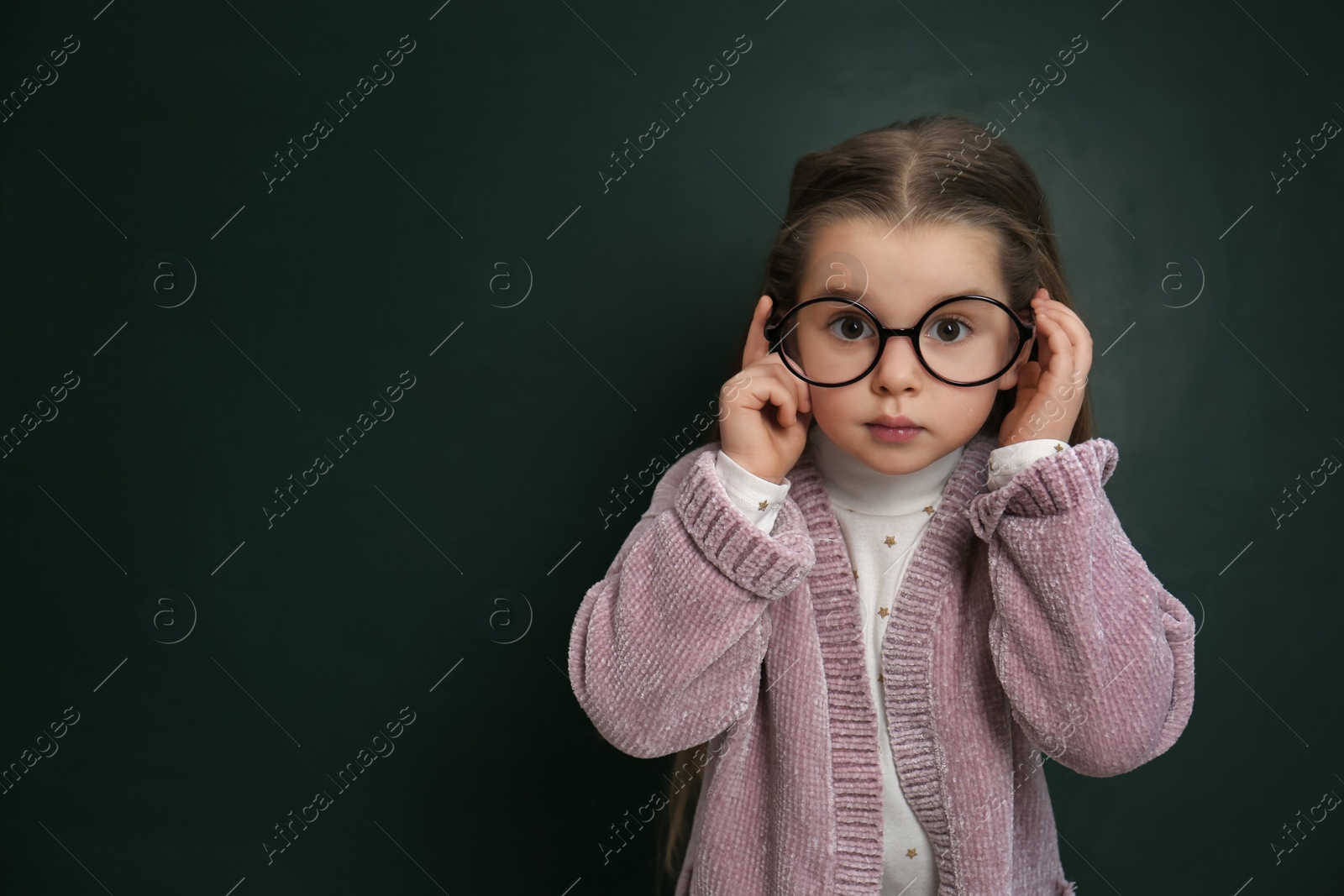 Photo of Cute little child wearing glasses near chalkboard, space for text. First time at school