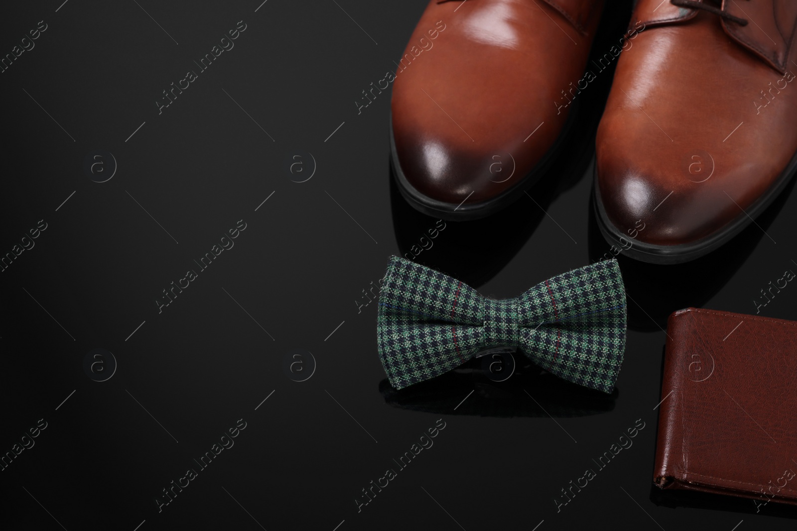 Photo of Stylish green checkered bow tie, wallet and shoes on black surface, space for text