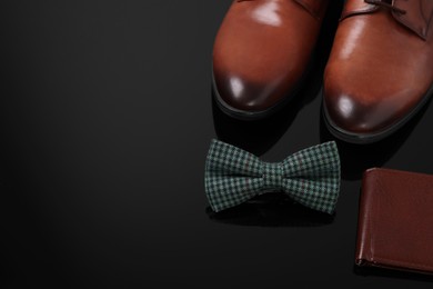 Stylish green checkered bow tie, wallet and shoes on black surface, space for text