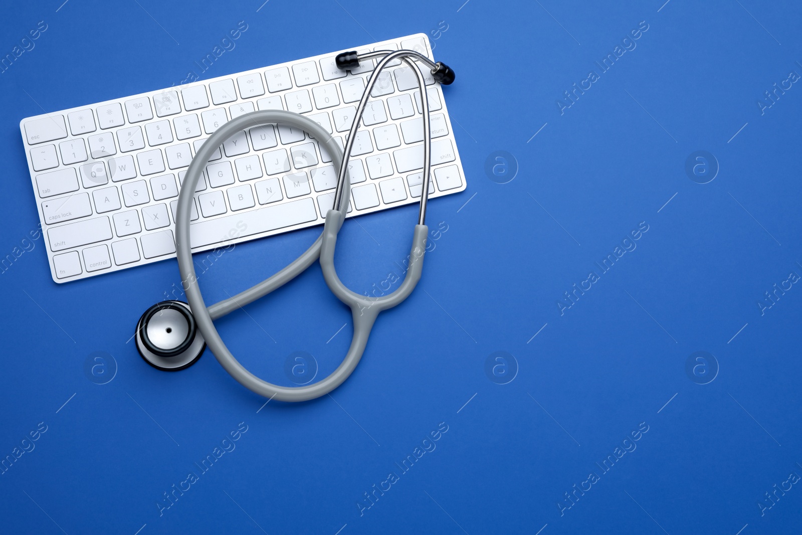 Photo of Computer keyboard with stethoscope on blue background, top view. Space for text