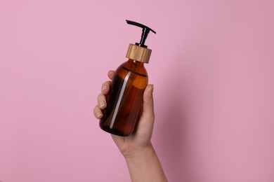 Woman holding bottle of cosmetic product on pink background, closeup