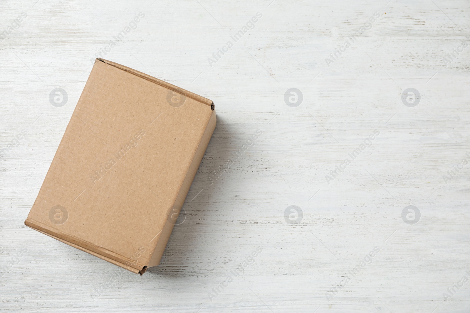 Photo of Cardboard box on white wooden background, top view. Space for text