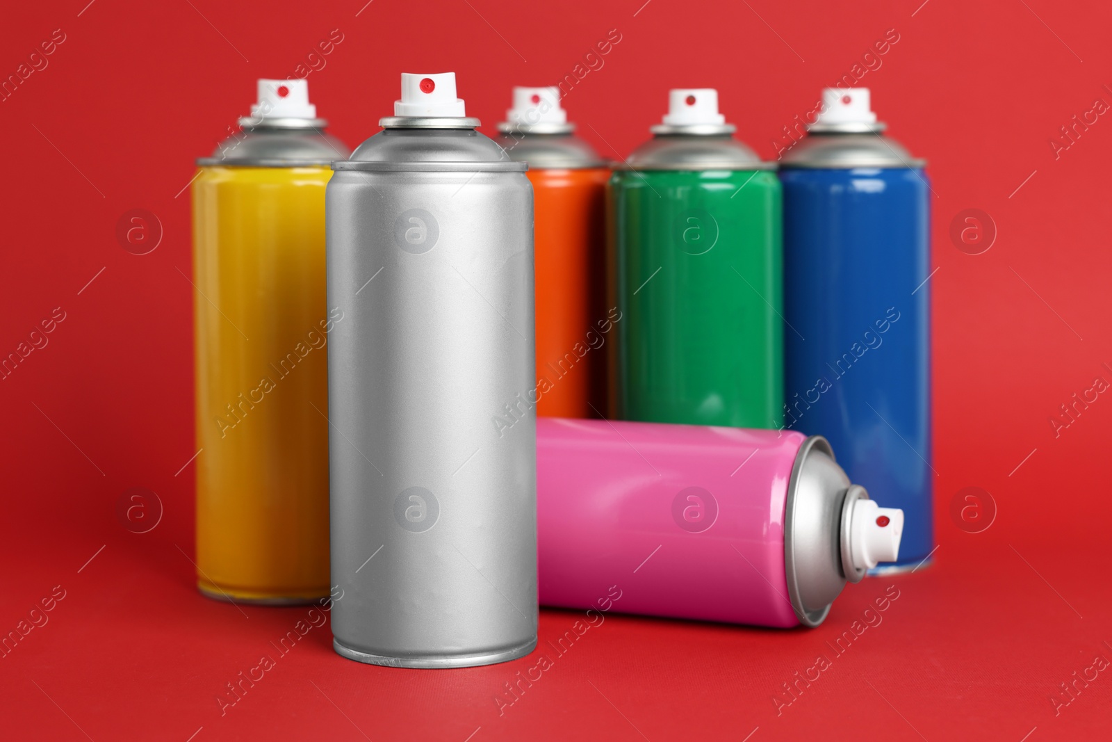 Photo of Colorful cans of spray paints on red background