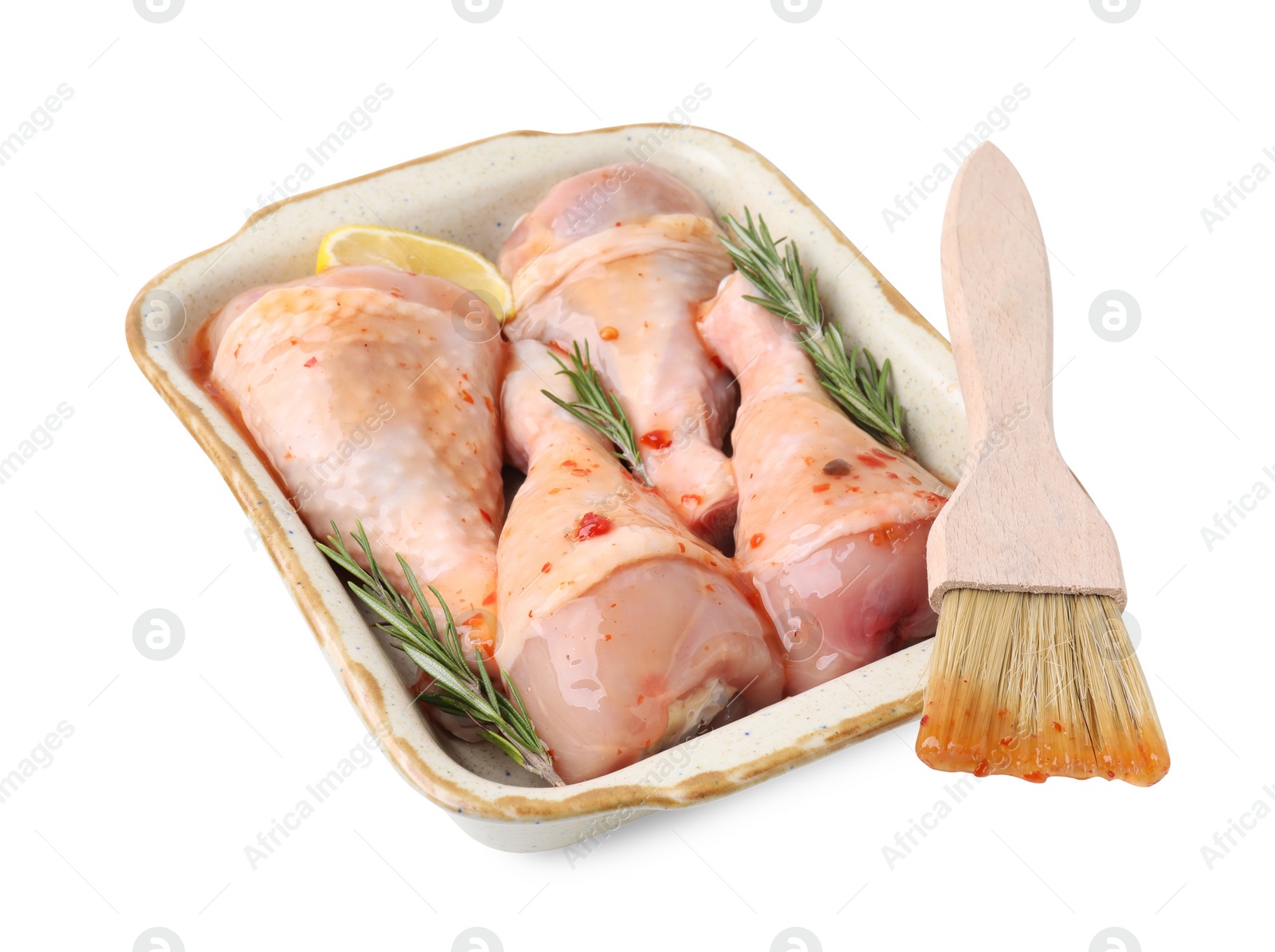 Photo of Raw marinated chicken drumsticks with rosemary, lemon and basting brush isolated on white