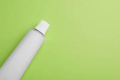 Blank white tube of ointment on light green background, top view. Space for text