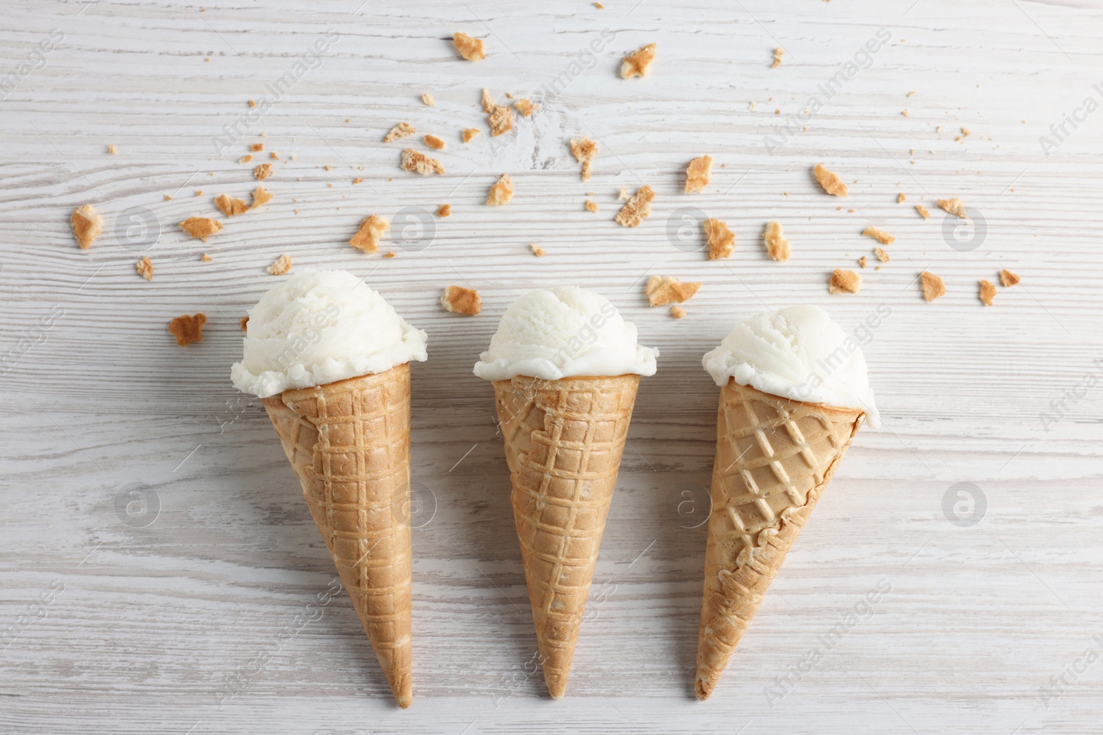 Photo of Ice cream scoops in wafer cones on light wooden table, flat lay