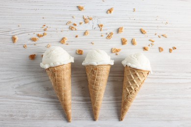 Ice cream scoops in wafer cones on light wooden table, flat lay