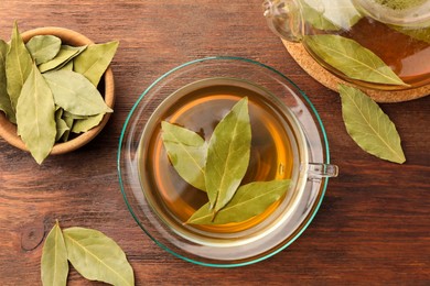 Photo of Cup of freshly brewed tea with bay leaves on wooden table, flat lay