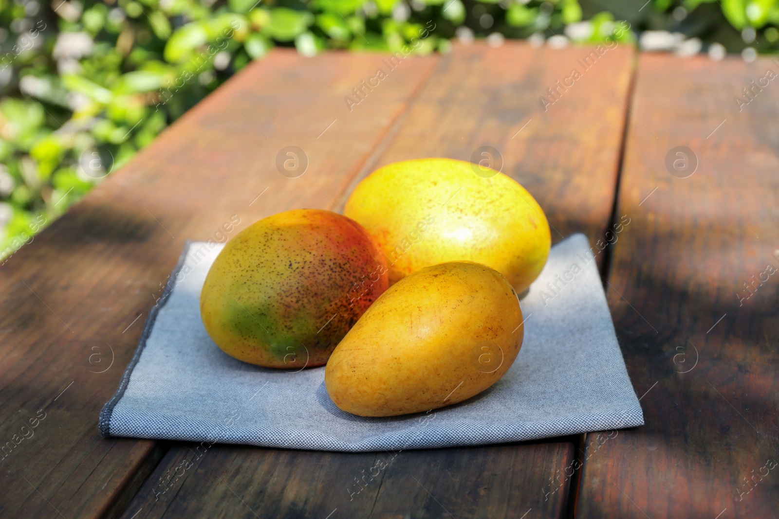 Photo of Many tasty mango fruits on wooden table outdoors