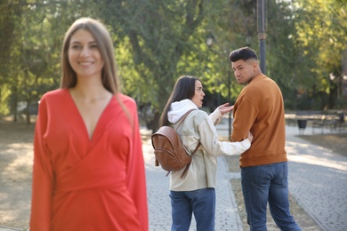 Disloyal man looking at another woman while walking with his girlfriend in park