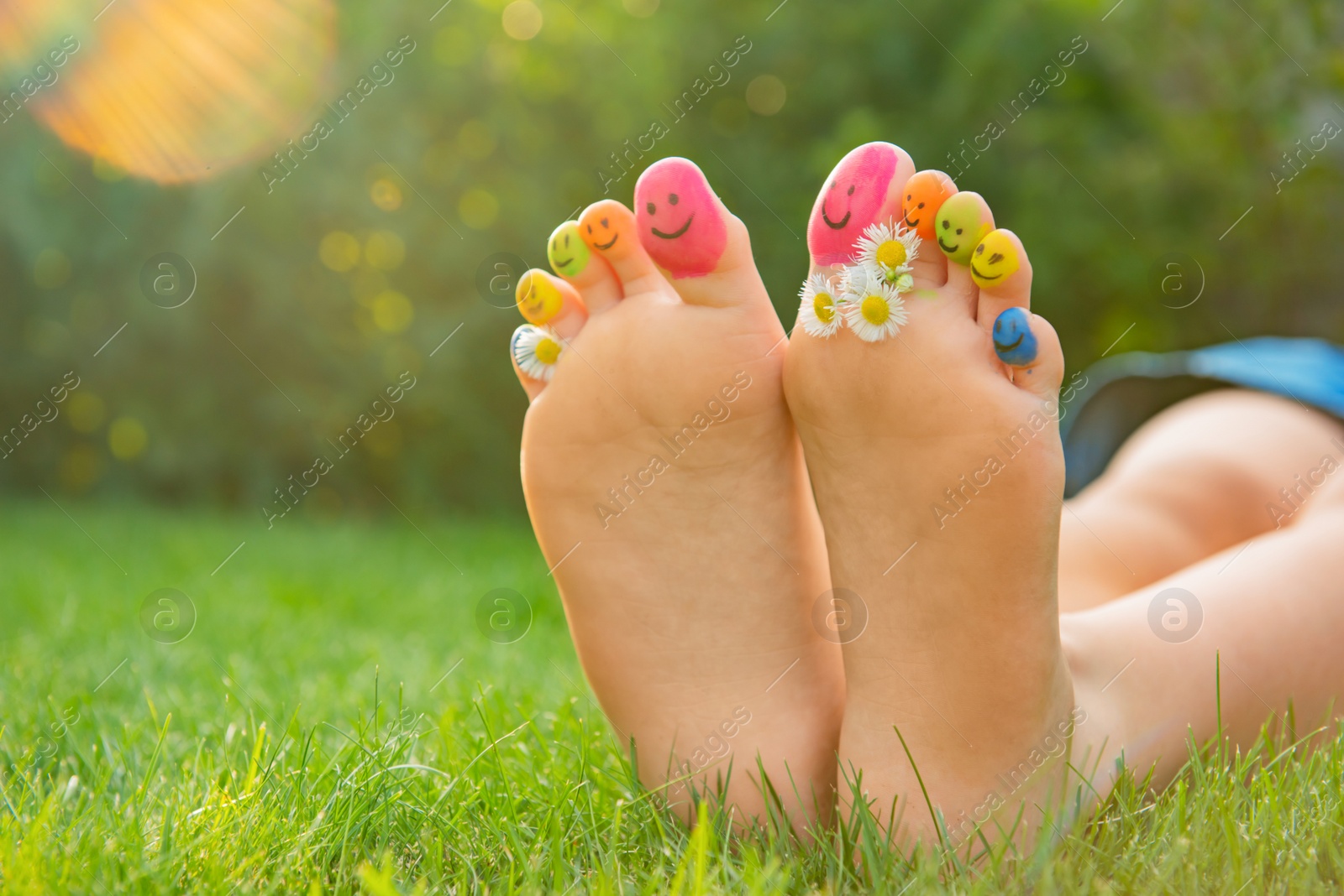 Photo of Teenage girl with chamomiles and smiling faces drawn on toes outdoors, closeup. Space for text