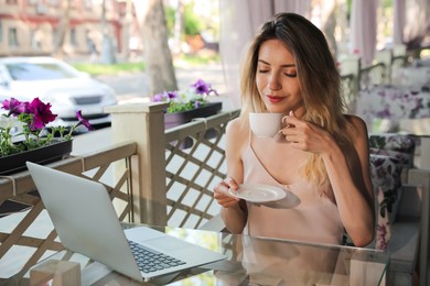 Photo of Happy young woman with cup of coffee and laptop enjoying early morning on cafe terrace