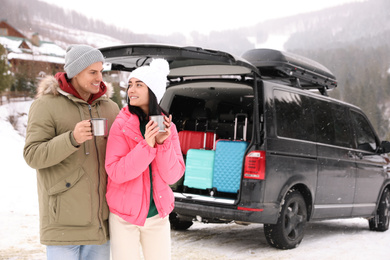 Photo of Happy couple with drinks near car on snowy road. Winter vacation