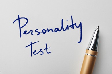 Text Personality Test and pen on white paper, top view