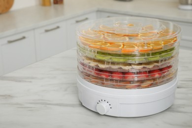 Dehydrator machine with different fruits and berries on white marble table in kitchen, space for text