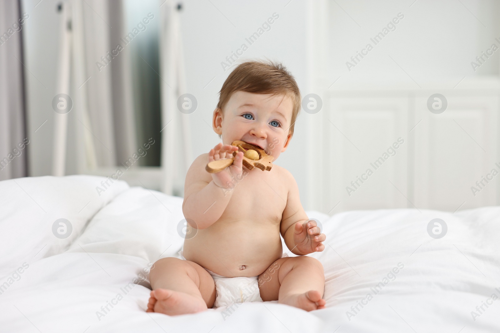 Photo of Cute baby boy with wooden rattle on bed at home