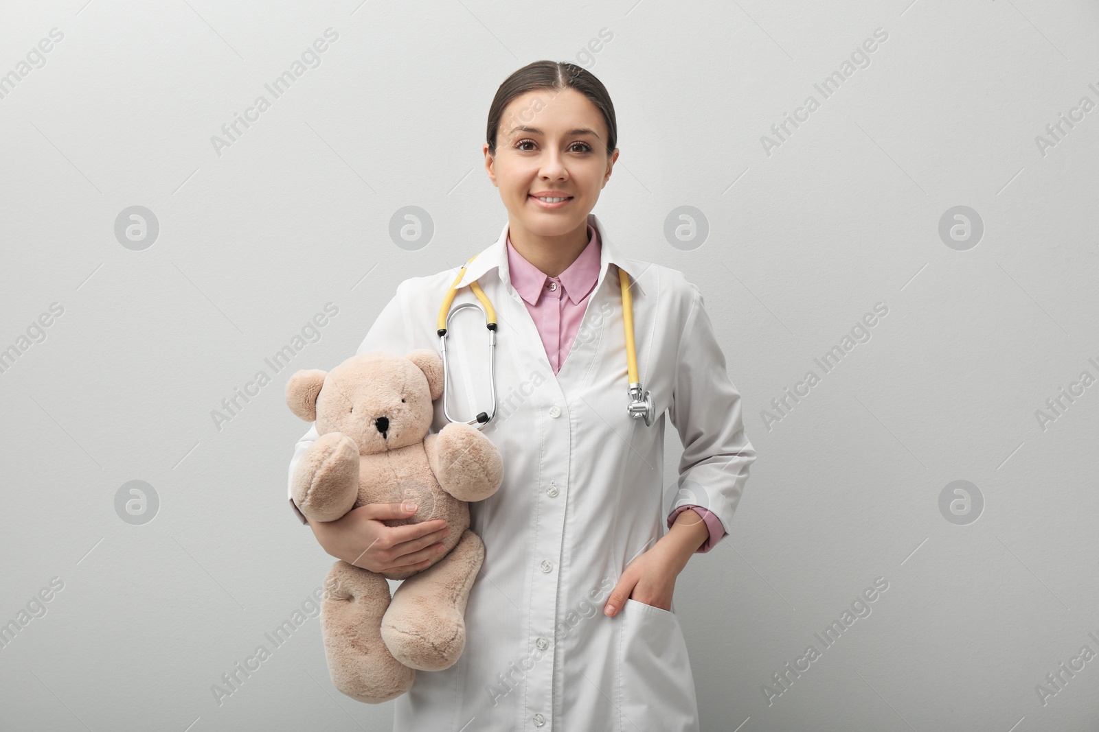 Photo of Pediatrician with teddy bear and stethoscope on light grey background