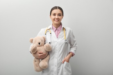Pediatrician with teddy bear and stethoscope on light grey background