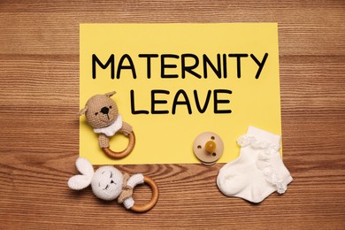 Photo of Baby socks, toys, pacifier and note with text Maternity Leave on wooden table, flat lay