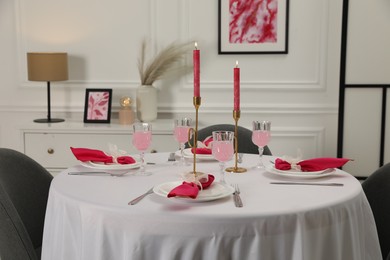 Photo of Color accent table setting. Glasses, plates, burning candles and pink napkins on table in dining room