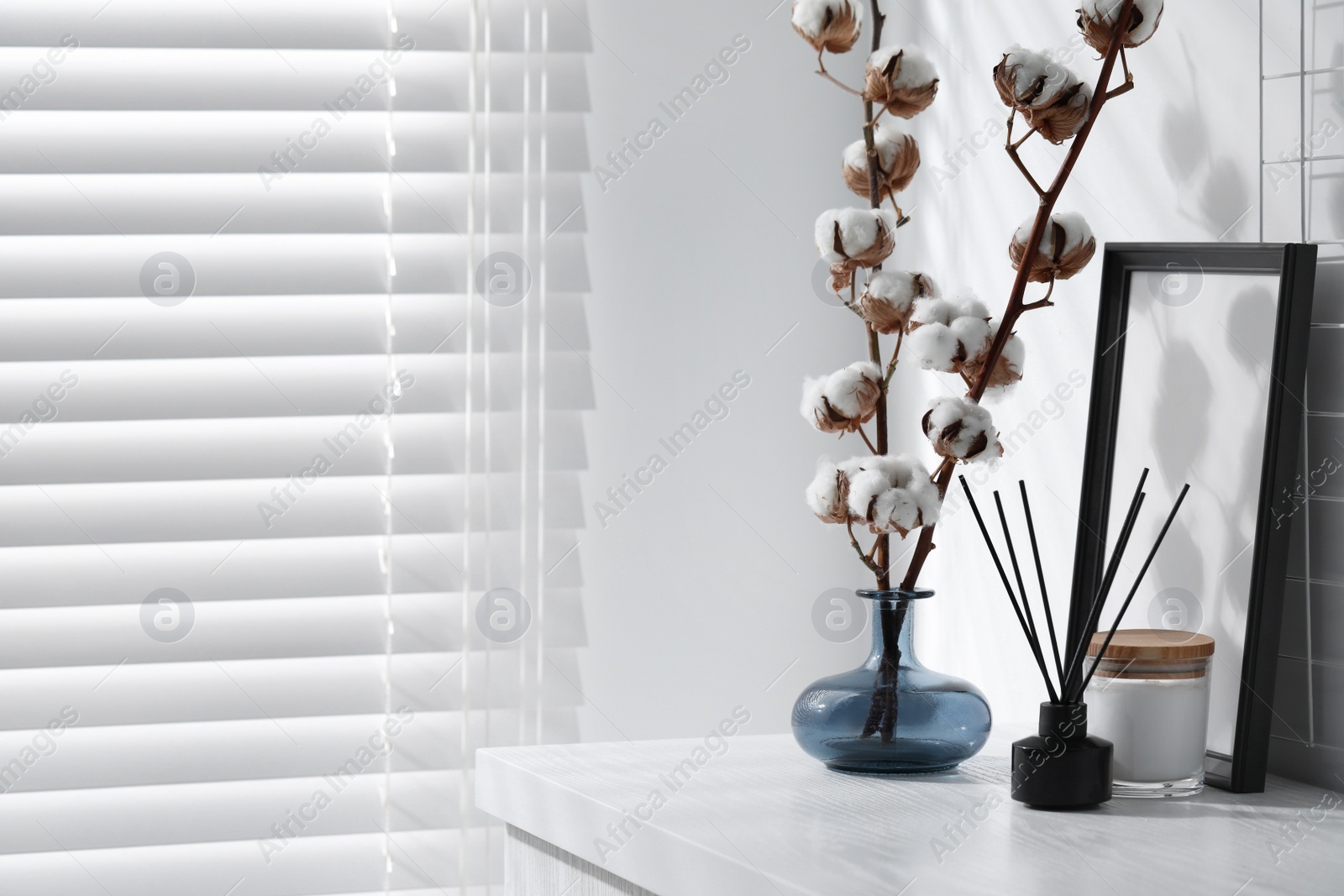 Photo of Reed diffuser, candle and cotton branches with fluffy flowers on white wooden table indoors. Space for text