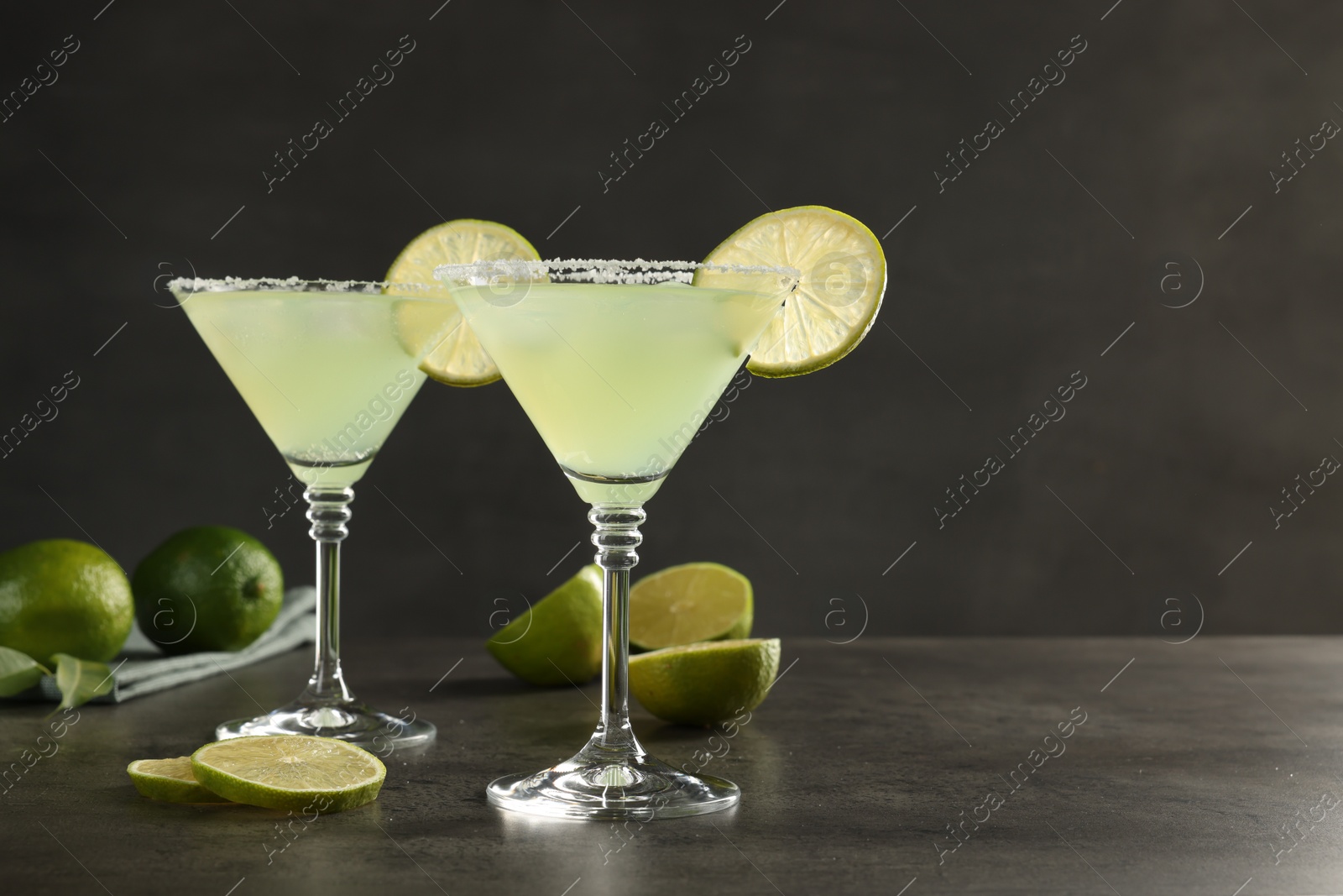 Photo of Delicious Margarita cocktail in glasses and limes on grey table, space for text