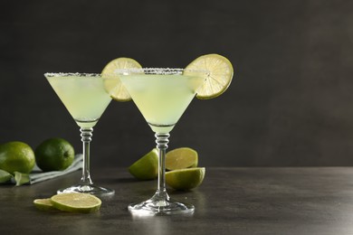 Delicious Margarita cocktail in glasses and limes on grey table, space for text