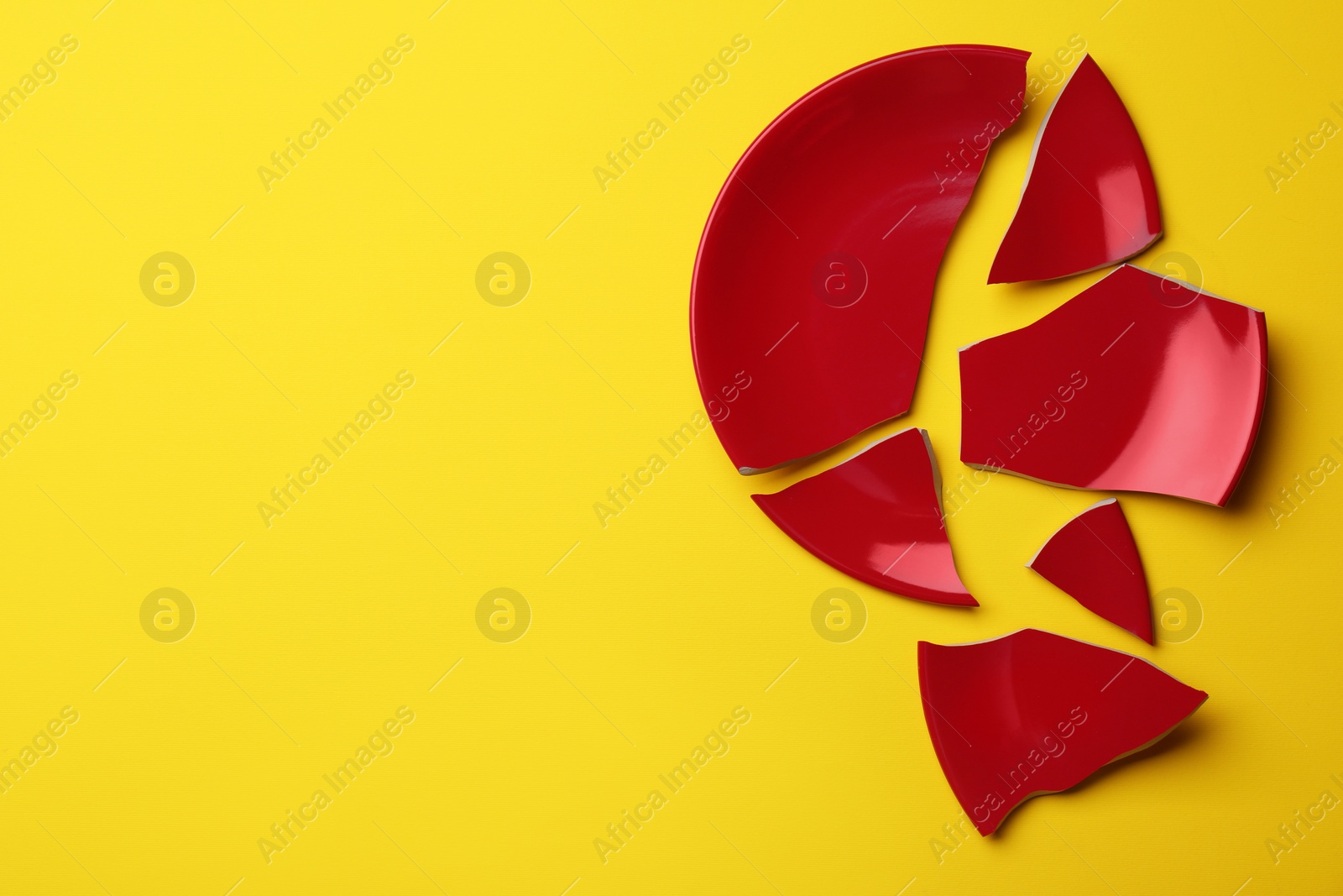 Photo of Pieces of broken red ceramic plate on yellow background, top view. Space for text