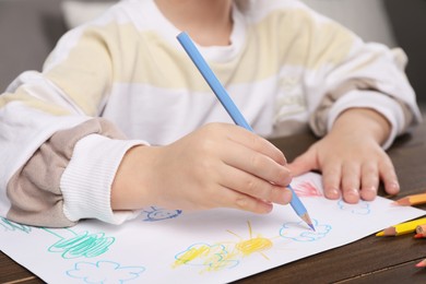 Photo of Little boy drawing with pencil at wooden table indoors, closeup. Child`s art