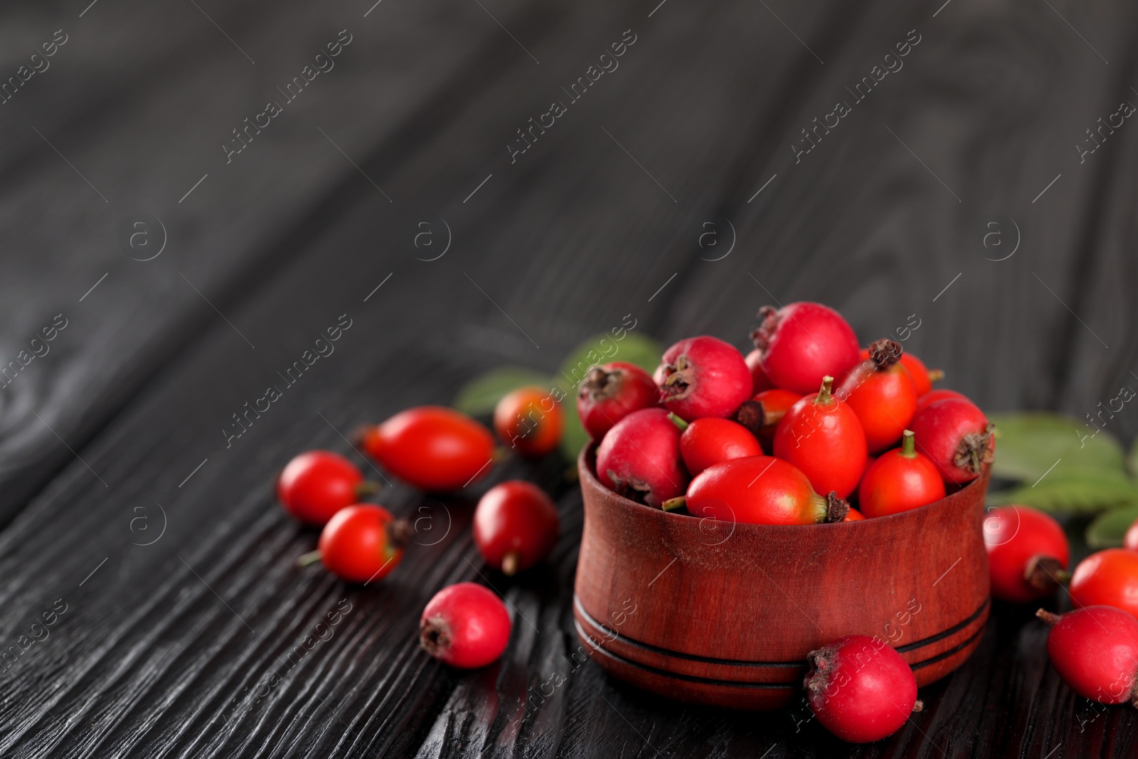 Photo of Ripe rose hip berries with green leaves on black wooden table. Space for text