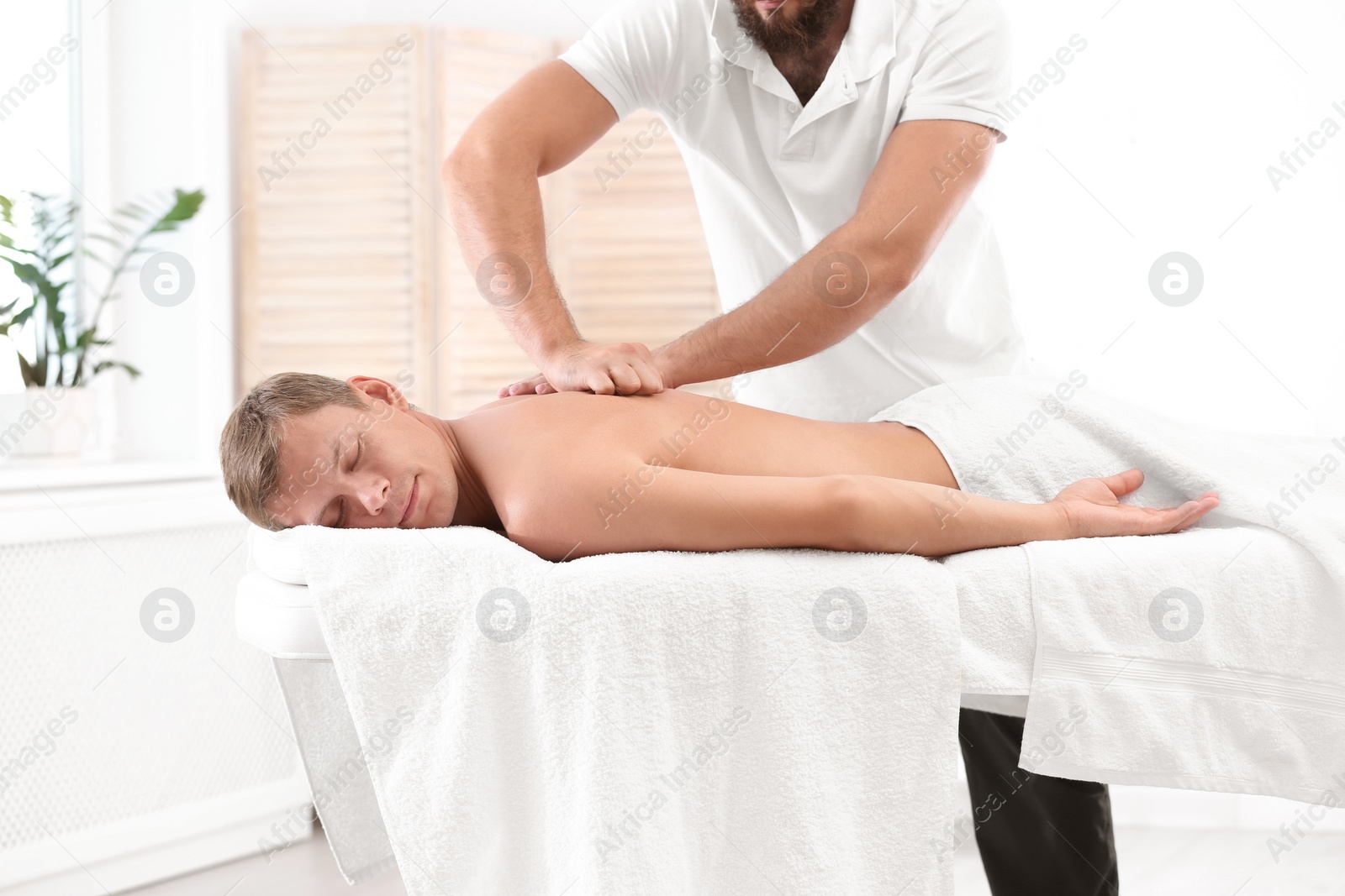 Photo of Relaxed man receiving back massage in wellness center