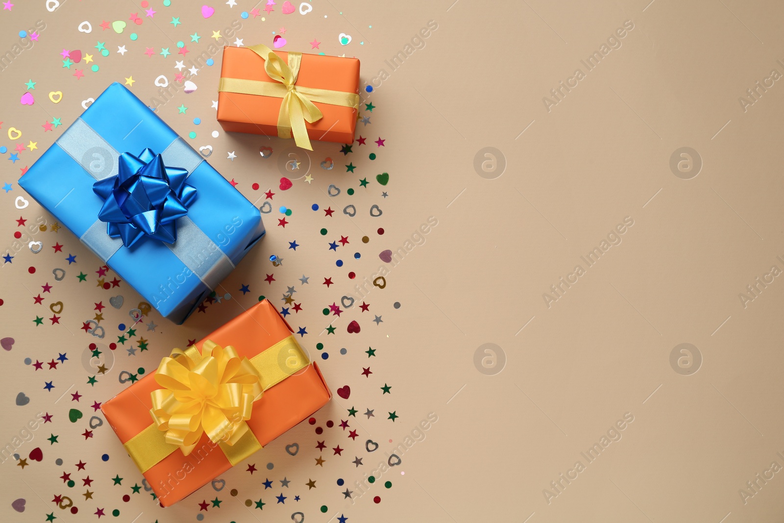 Photo of Gift boxes and shiny confetti on beige background, flat lay. Space for text