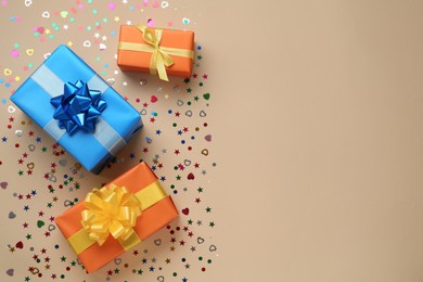 Gift boxes and shiny confetti on beige background, flat lay. Space for text