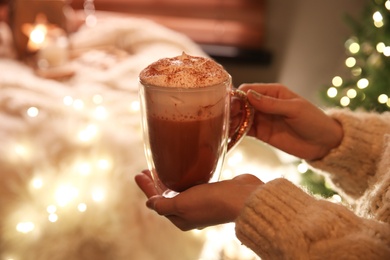 Photo of Woman holding cup of delicious drink with whipped cream indoors, closeup. Christmas celebration