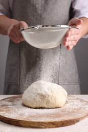 Photo of Man sprinkling flour over dough at table near grey wall, closeup