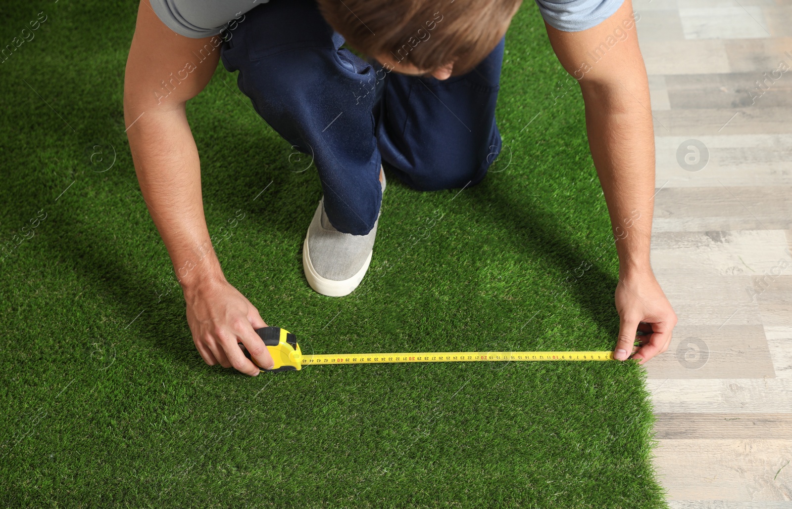 Photo of Man measuring artificial grass carpet indoors, above view