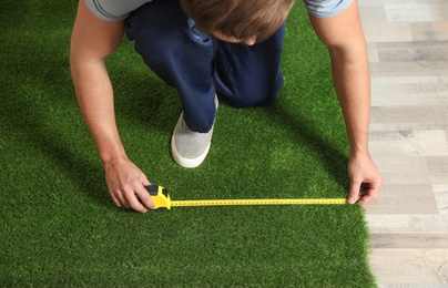 Man measuring artificial grass carpet indoors, above view