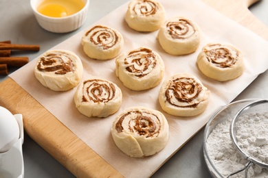 Photo of Wooden board with raw cinnamon rolls on table
