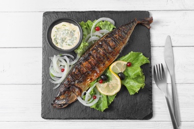 Photo of Slate plate with delicious grilled fish and sauce on wooden table, top view