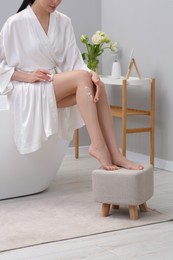 Photo of Woman applying body cream onto her smooth legs in bathroom, closeup