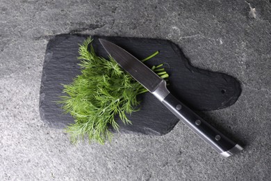 Sprigs of fresh green dill and knife on grey table, top view