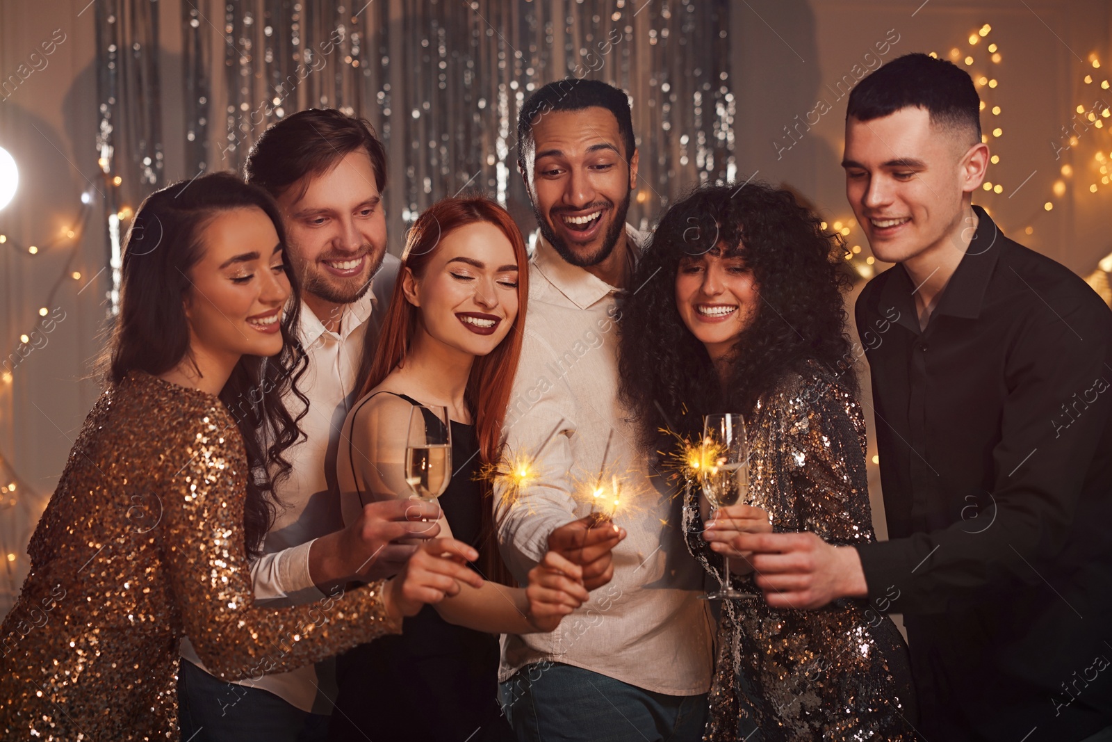 Photo of Happy friends with glasses of wine and sparklers celebrating birthday indoors