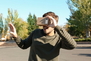 Young man using cardboard virtual reality headset outdoors