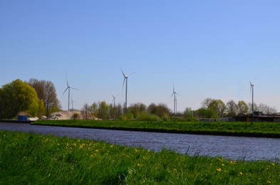 Photo of Beautiful view of countryside with river and wind turbines on sunny day. Alternative energy source