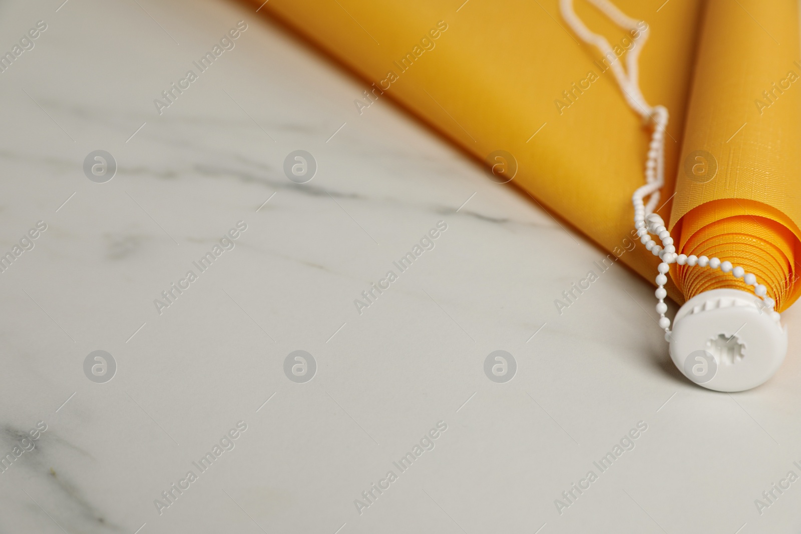 Photo of Stylish roller window blinds on white marble table, closeup. Space for text